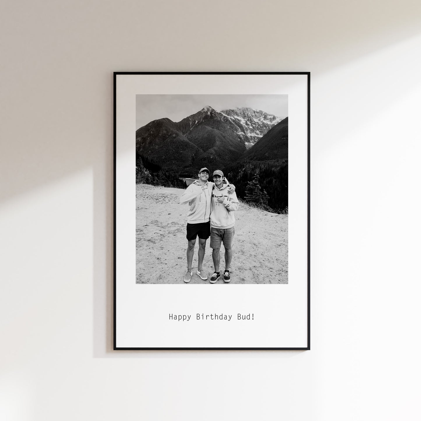 Custom Print Featuring black and white photo sent in by the customer, with custom text below reading "Happy Birthday Bud". Photo included features 2 men with arms around eachother. Perfect gift for him. Print is framed and hung up on white wall.