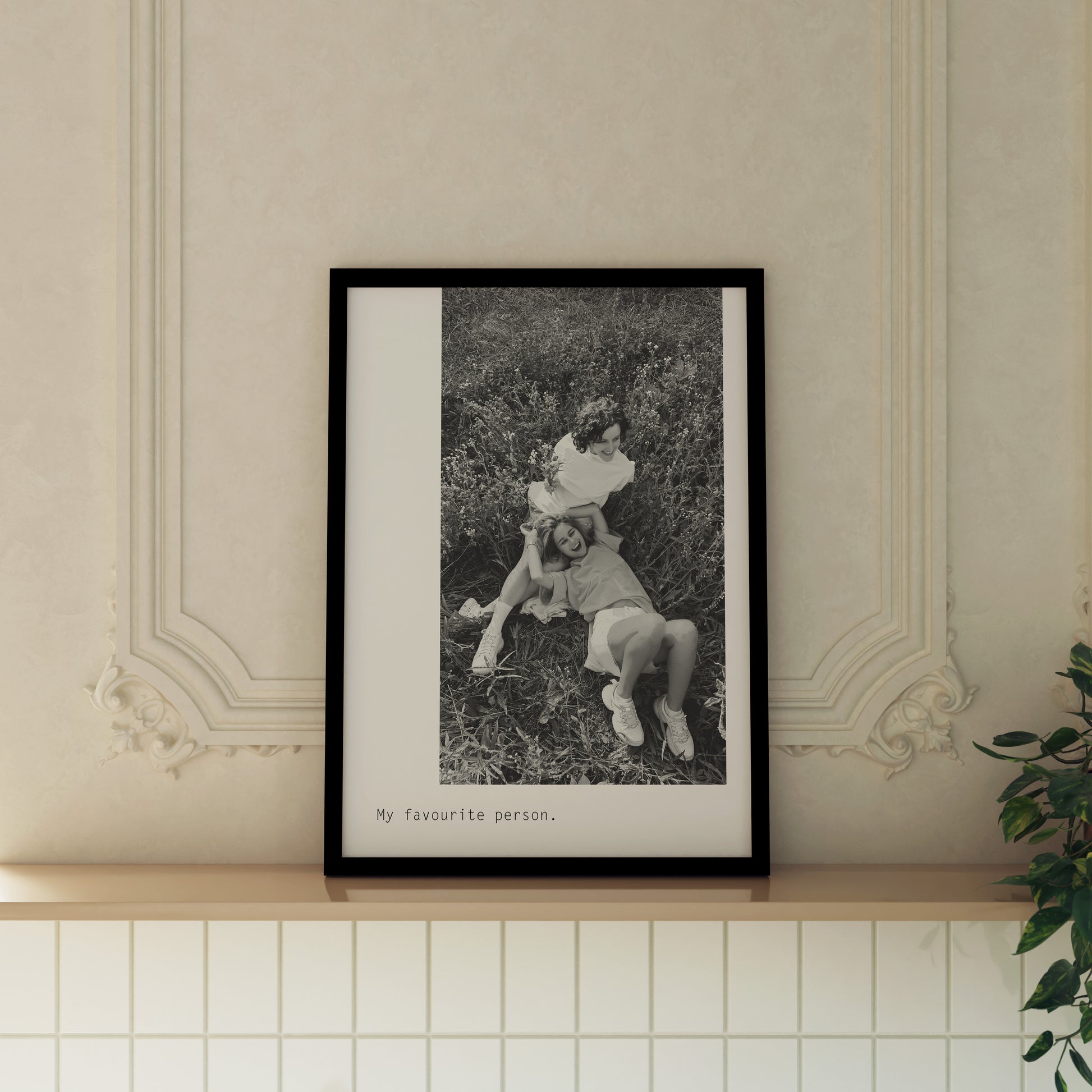 Large Photo Custom Monochrome Happy Birthday Print featuring custom photo of 2 girls laughing on the floor. Below is custom text sent in by the customer, reading My Favourite Person. Print is framed in black frame and displayed in expensive looking house on wooden ledge