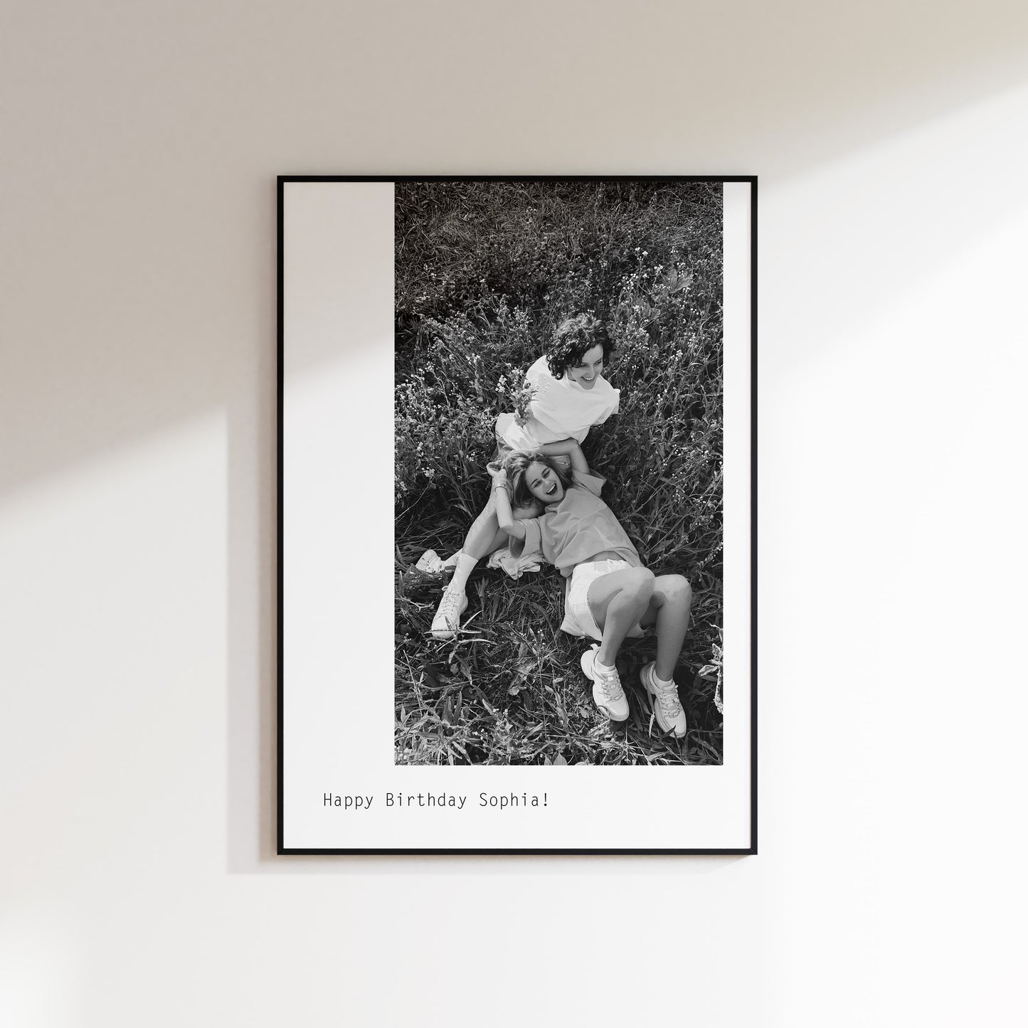 Custom Print with large black and white offset image sent in by customer. Photo here features 2 girls laughing together. Below is custom happy birthday text. The Print is framed in a black frame and hung on a wall.