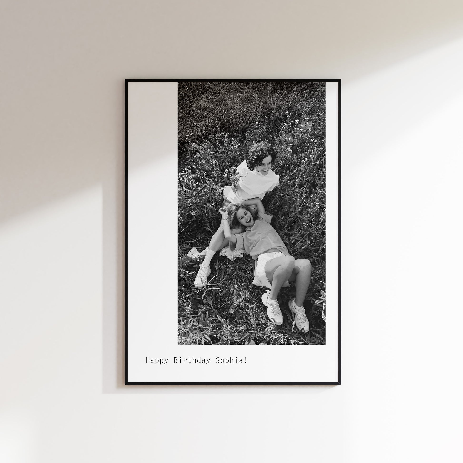 Custom Print with large black and white offset image sent in by customer. Photo here features 2 girls laughing together. Below is custom happy birthday text. The Print is framed in a black frame and hung on a wall.