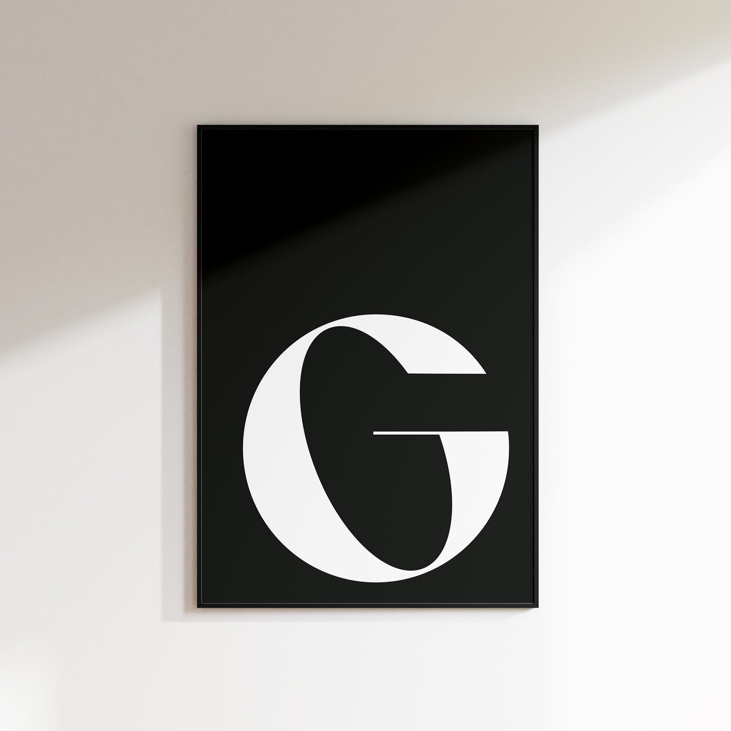 An initial print for the home, ideal for hallways, living rooms and bedrooms. This is a slate coloured print with a white uppercase ‘G’ in a high contrast serif typeface. Print is in a black frame on a white wall background.