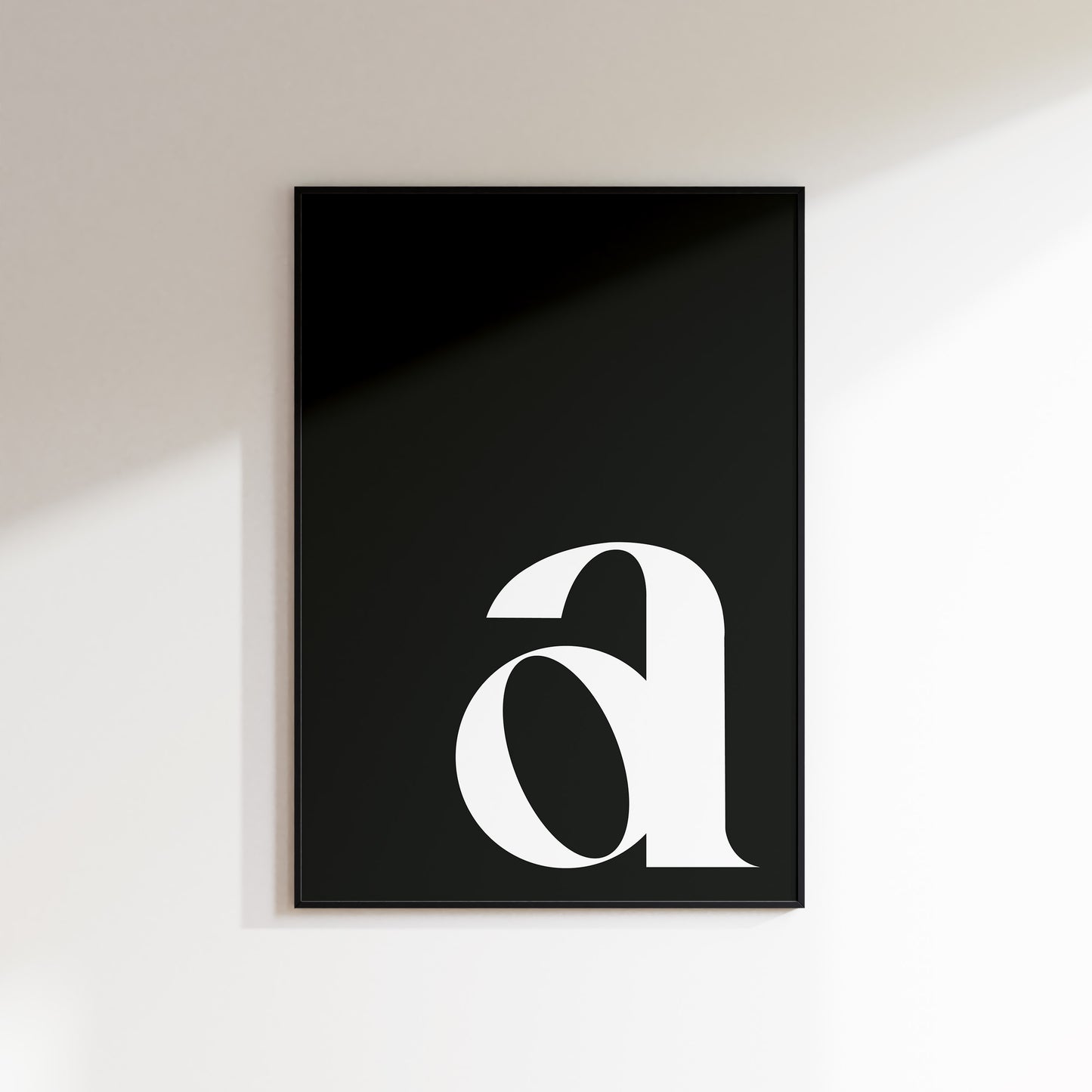 An initial print for the home, ideal for hallways, living rooms and bedrooms. This is a slate coloured print with a white lowercase ‘a’ in a high contrast serif typeface. Print is in a black frame on a white wall background.