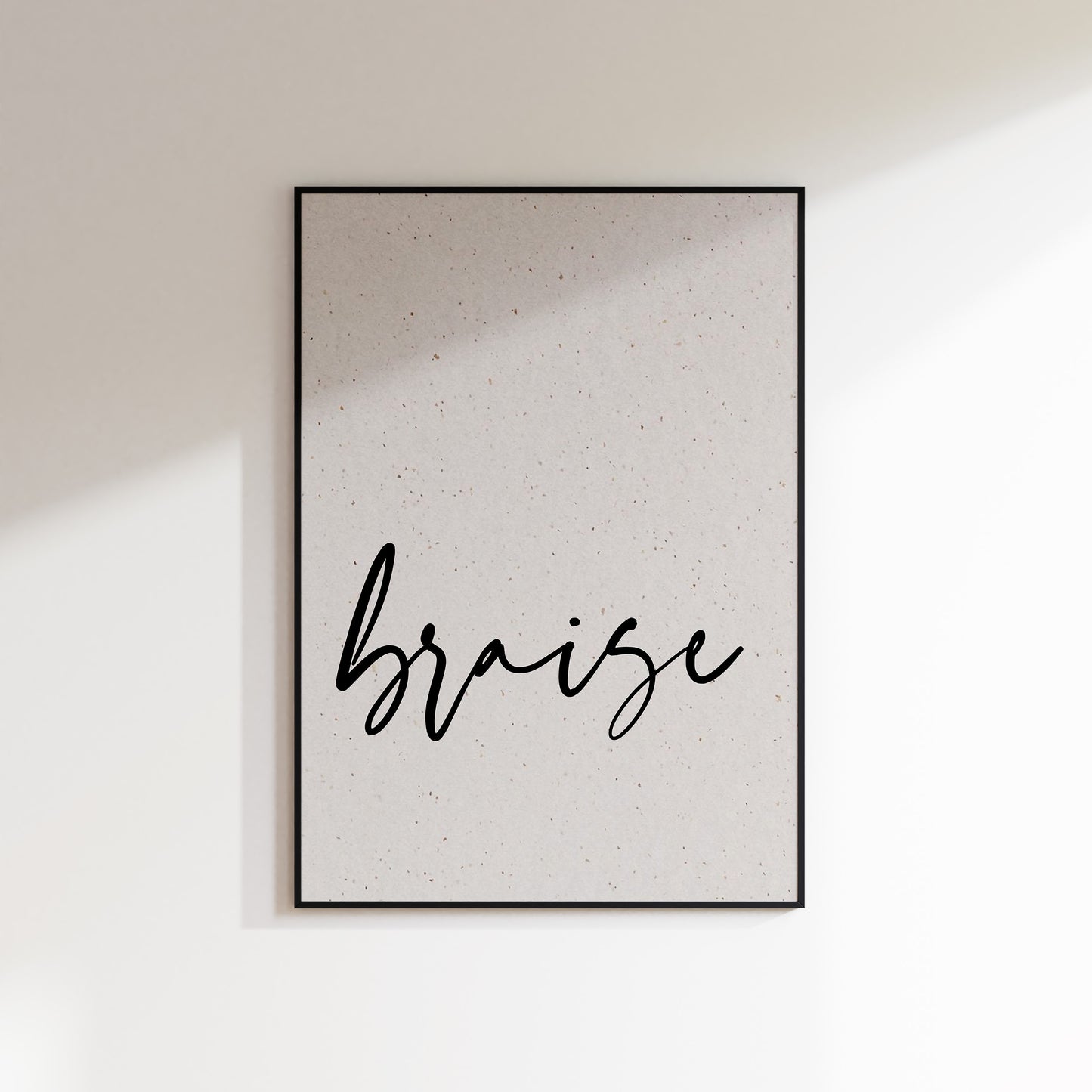 A print on textured paper with black text that reads 'braise' in a handwriting style typeface. A culinary print for the kitchen. Print is in a black frame on a white wall background.
