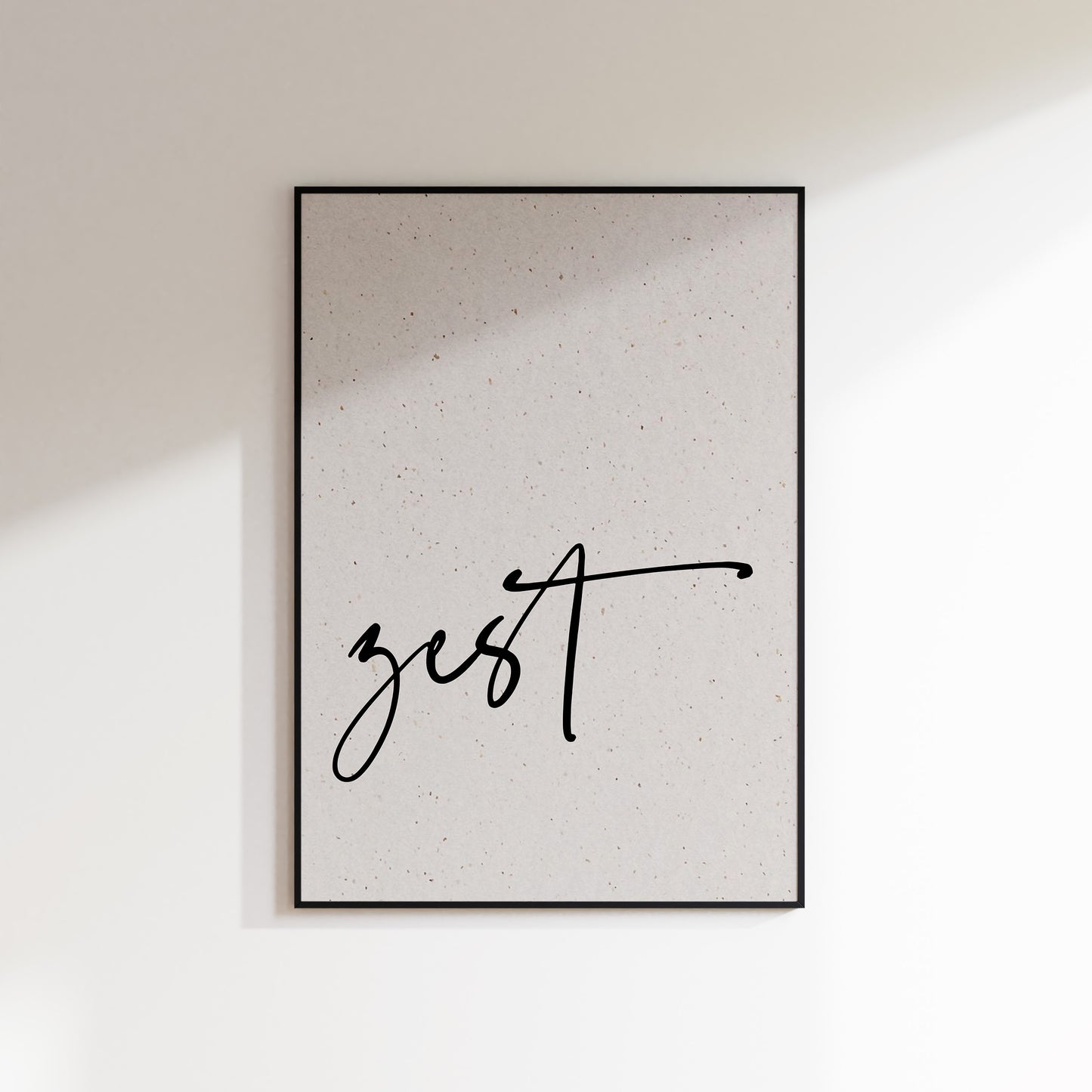 A print on textured paper with black text that reads 'zest' in a handwriting style typeface. A culinary print for the kitchen. Print is in a black frame on a white wall background.
