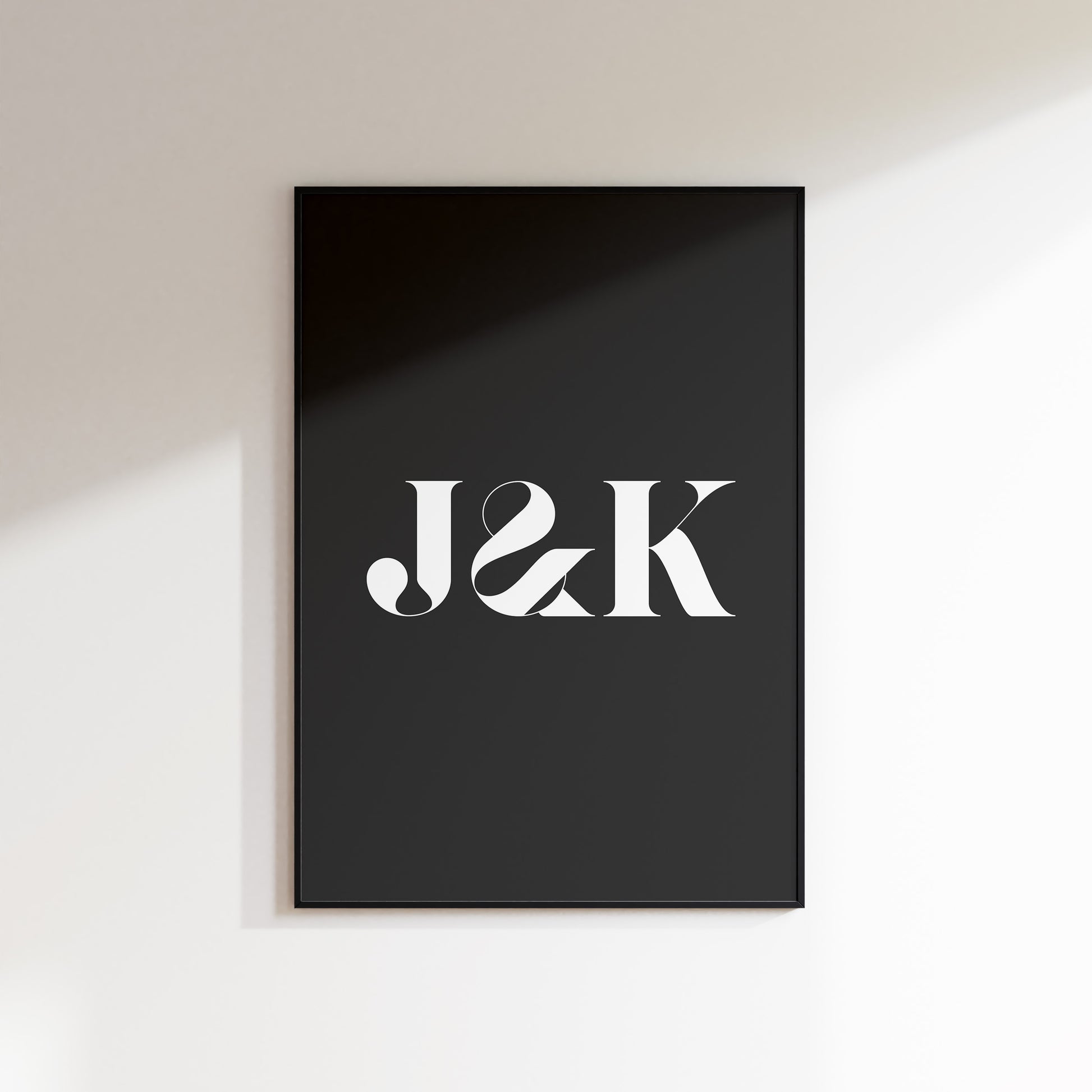 An initials print for the home, ideal for hallways, living rooms and bedrooms. This is a slate coloured print with a white uppercase ‘J & K’ in a high contrast serif typeface. Print is in a black frame on a white wall background.