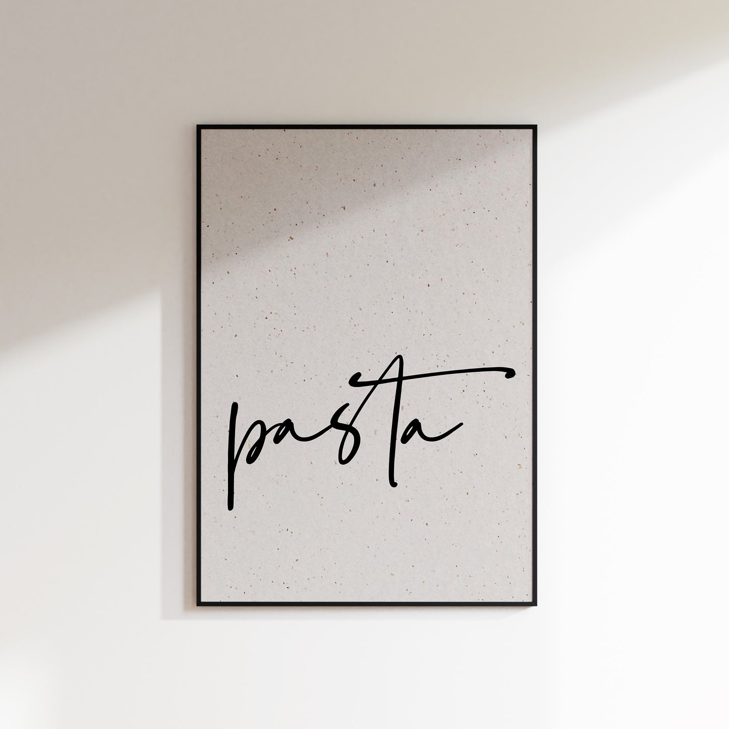 A print on textured paper with black text that reads 'pasta' in a handwriting style typeface. A culinary print for the kitchen. Print is in a black frame on a white wall background.