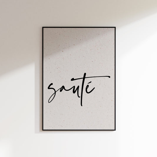 A print on textured paper with black text that reads 'sauté' in a handwriting style typeface. A culinary print for the kitchen. Print is in a black frame on a white wall background.