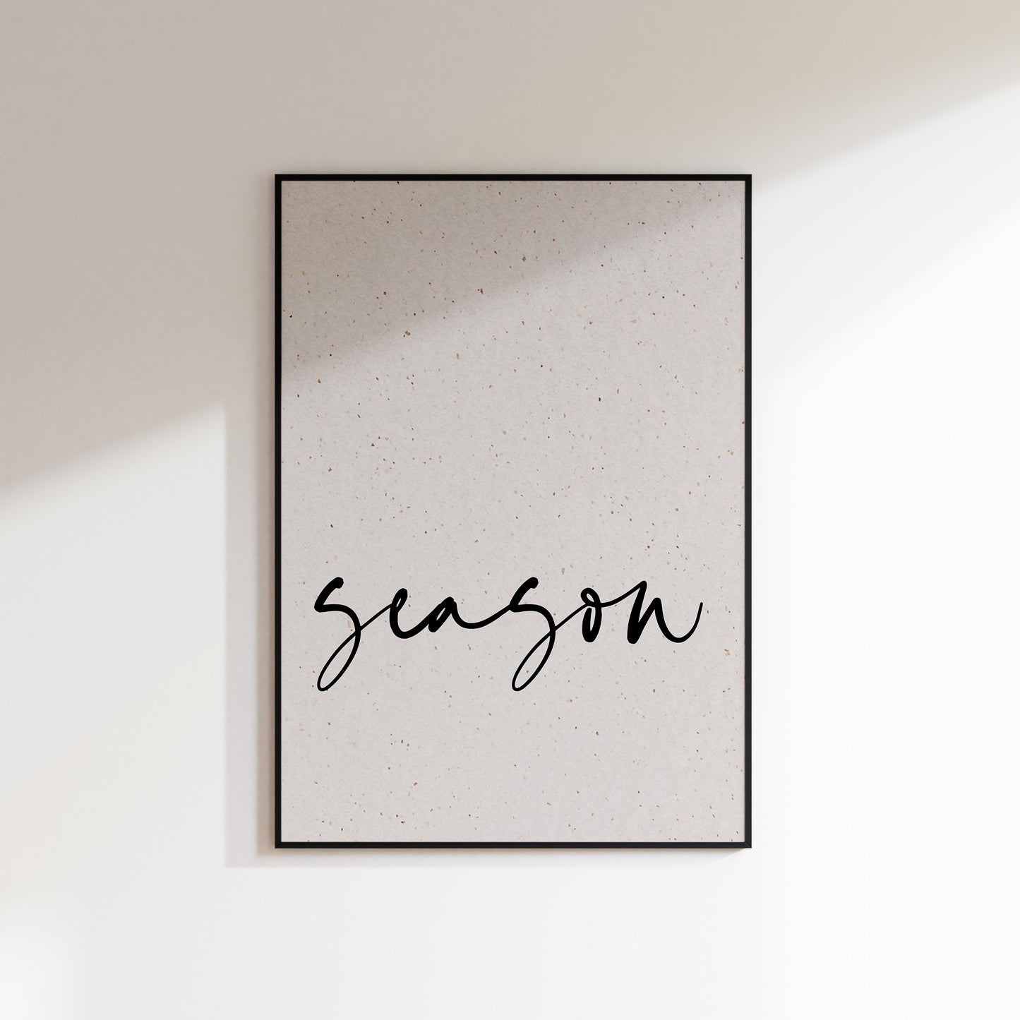 A print on textured paper with black text that reads 'season' in a handwriting style typeface. A culinary print for the kitchen. Print is in a black frame on a white wall background.