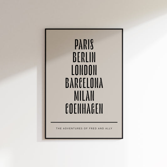 Six holiday destination print in beige with black type. Featuring Paris, Berlin, London, Barcelona, Milan and Copenhagen. Below the list of locations is the custom text "the adventures of fred and Ally. The Print is framed in a black frame and hung on a white wall