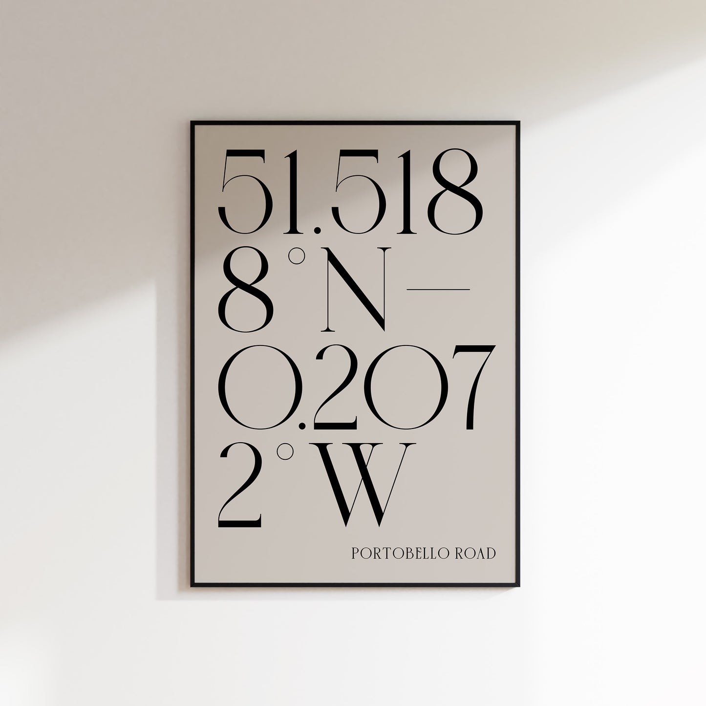 A Deco Style Coordinate Print in a black frame on a white wall background with shadow. This is a neutral beige coloured print with slate coloured number coordinates in a deco style serif typeface. 