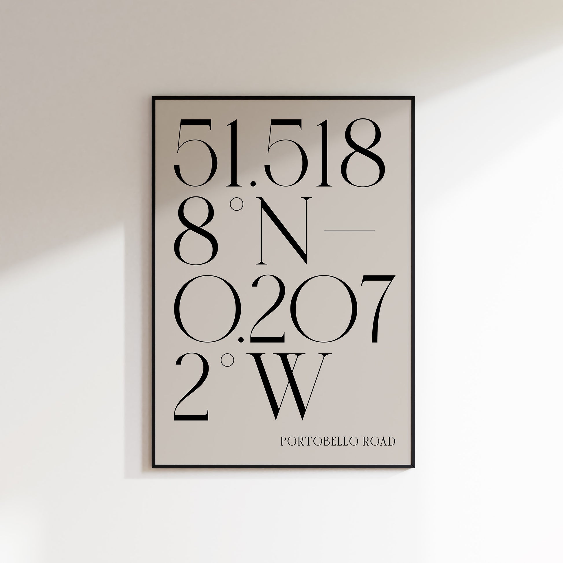A Deco Style Coordinate Print in a black frame on a white wall background with shadow. This is a neutral beige coloured print with slate coloured number coordinates in a deco style serif typeface. 